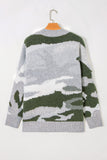 A knit crewneck sweater with a horizontal camouflage pattern in shades of gray, white, and dark olive green, hanging on a wooden hanger against a plain white wall.