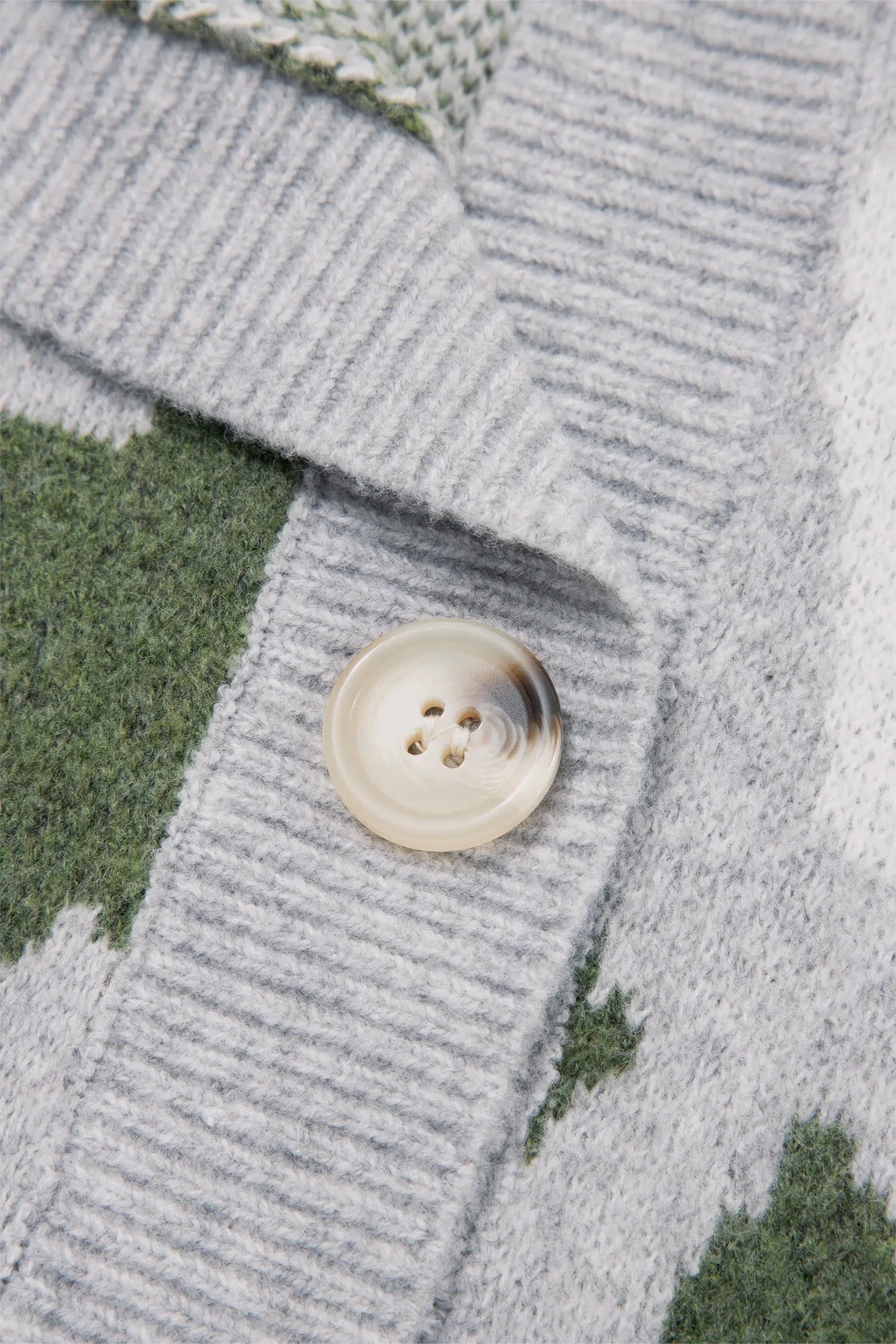 Close-up of a knit cardigan with a ribbed gray front panel, green geometric patterned sections, and a cream-colored button.