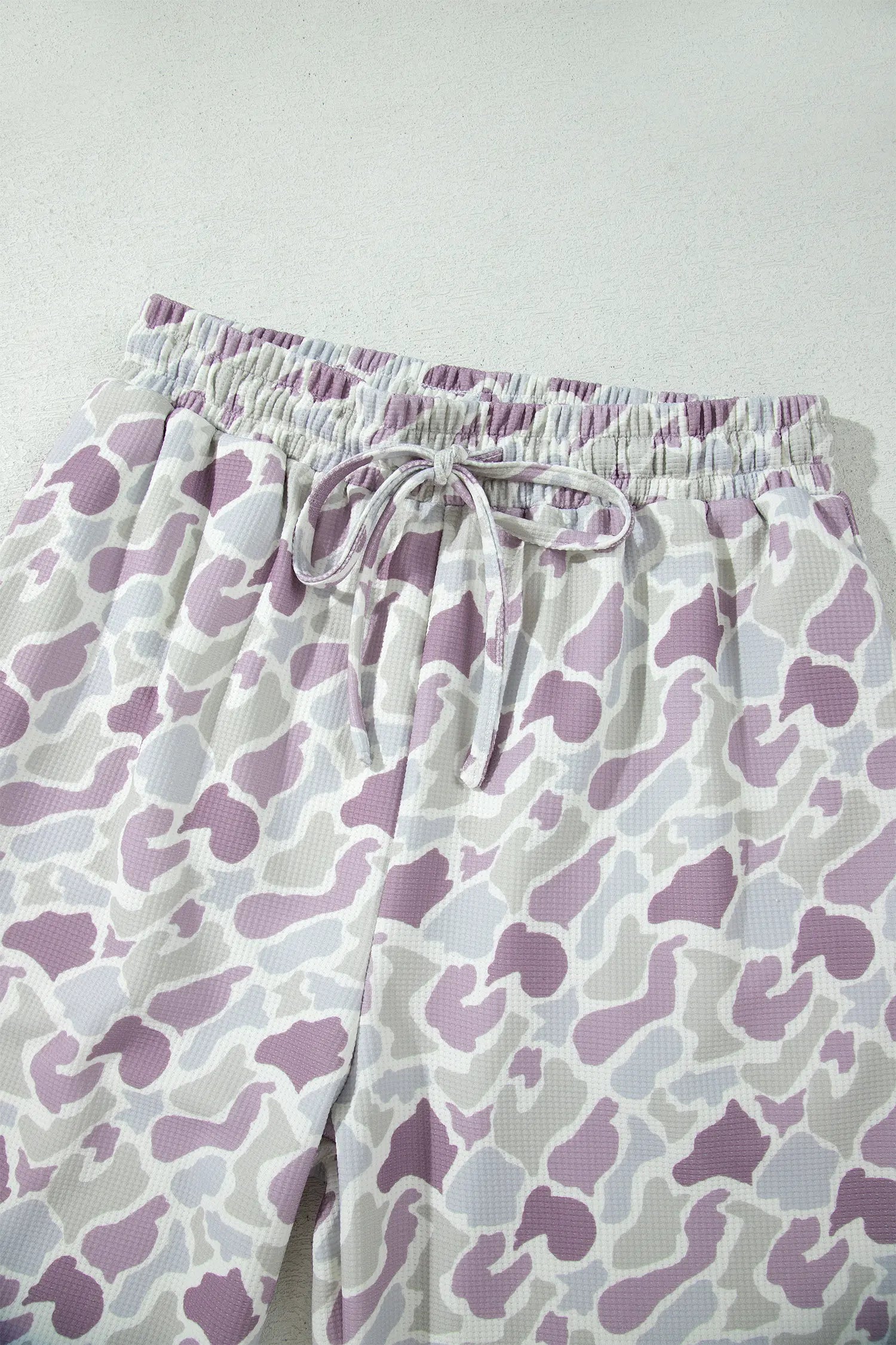 White drawstring shorts with a purple and gray abstract organic pattern, shown on a light gray background.