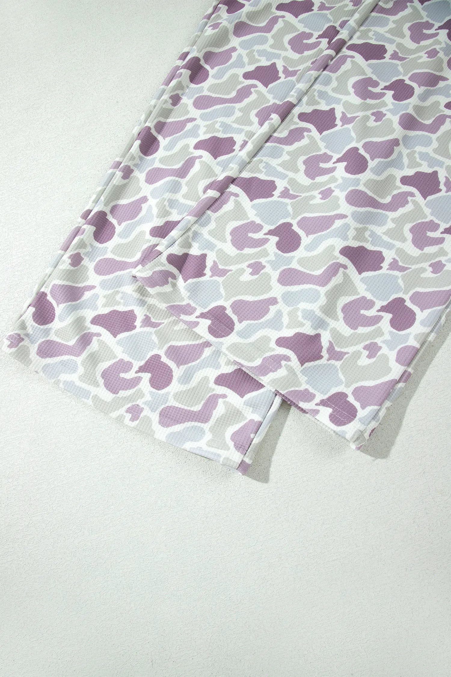 A close-up of a folded piece of fabric with a repeating abstract camouflage-like pattern in lavender purple, light gray, and white.