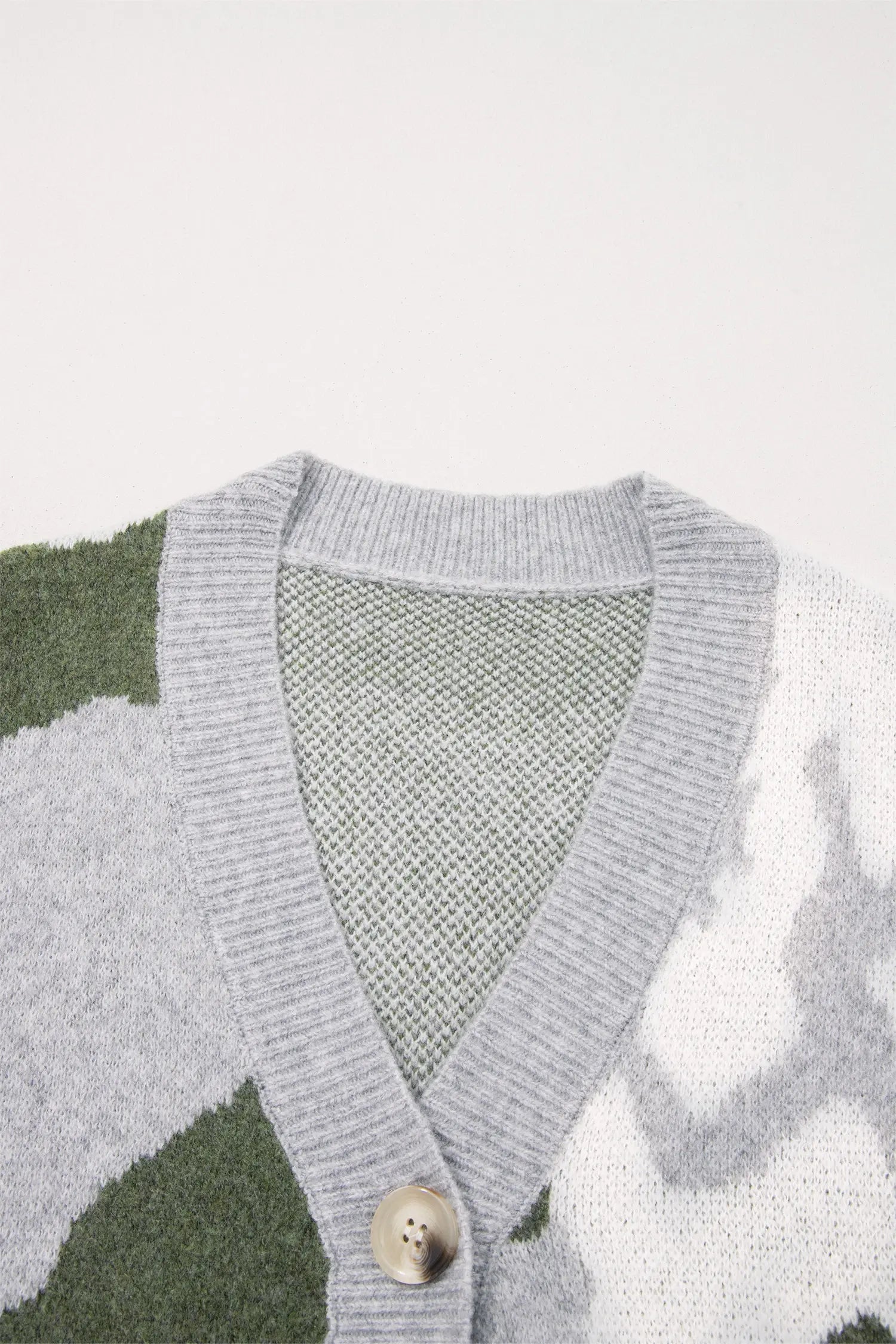 Close-up of a knit cardigan with a gray ribbed V-neck and button closure, featuring a green and white abstract pattern.