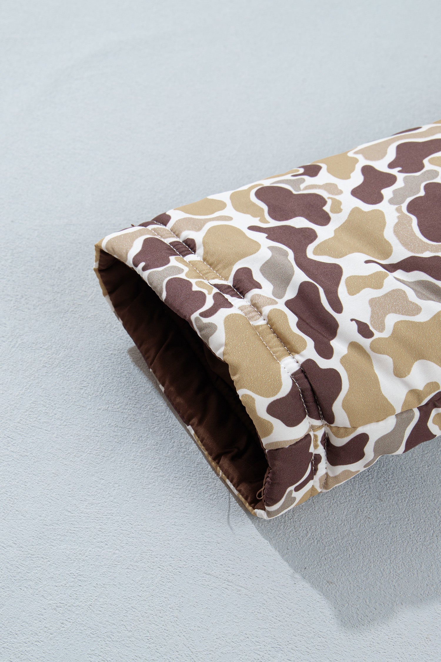 Close-up of brown, beige, and white camouflage quilted sleeve cuff on light gray background.