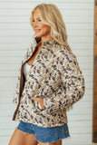 Woman in beige-brown camouflage high-collar jacket and denim shorts by a white wall.
