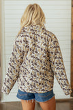 Back view of woman in brown, beige, white cow print quilted jacket with denim shorts.