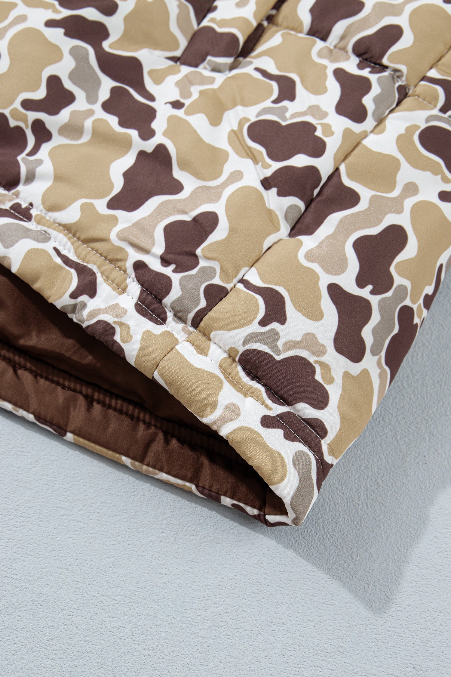 Close-up of brown, beige, and white camouflage quilted puffer jacket corner with solid brown lining.