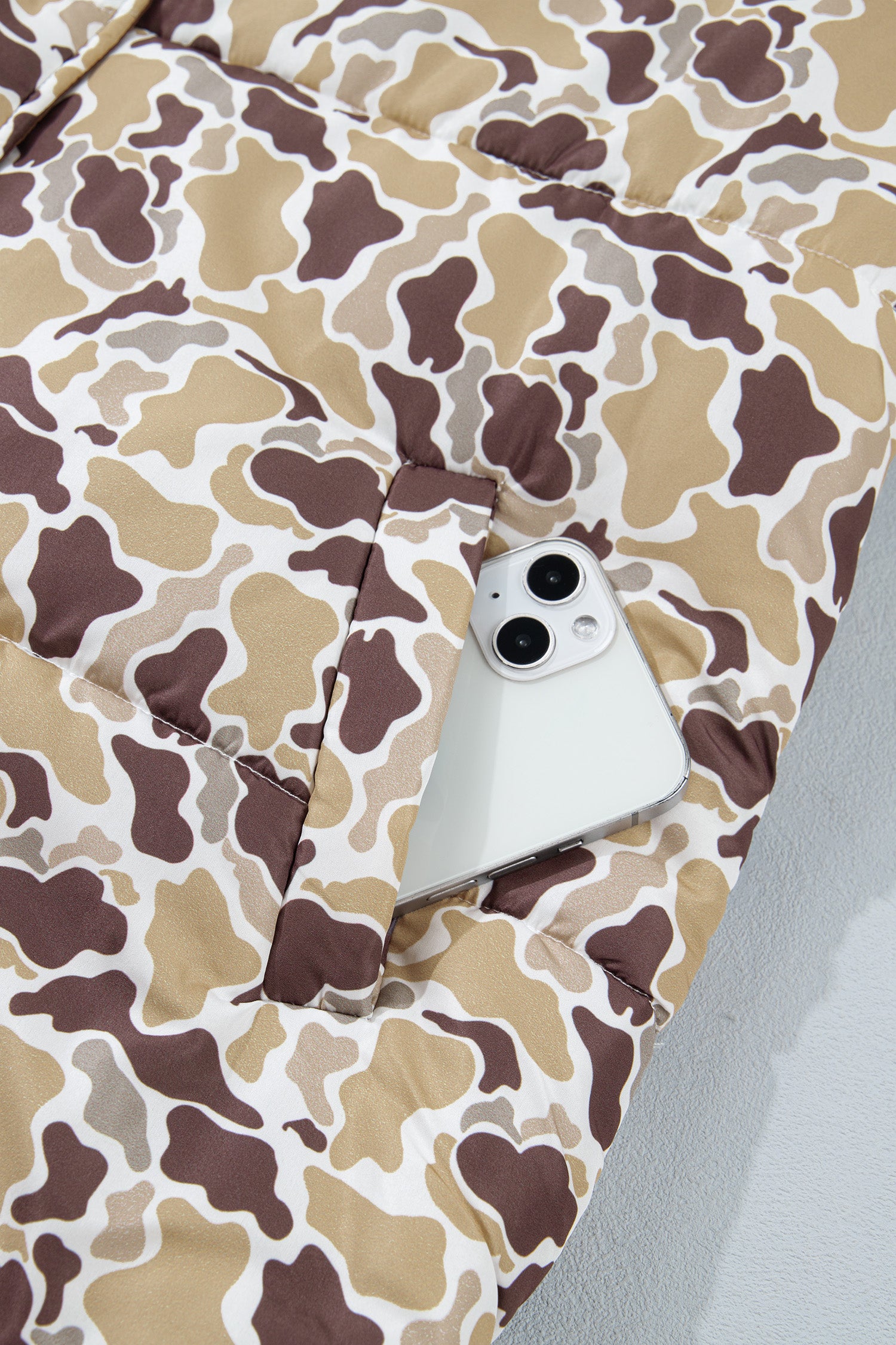 Close-up of brown, beige, and white cow-print quilted puffer jacket with white smartphone in pocket.
