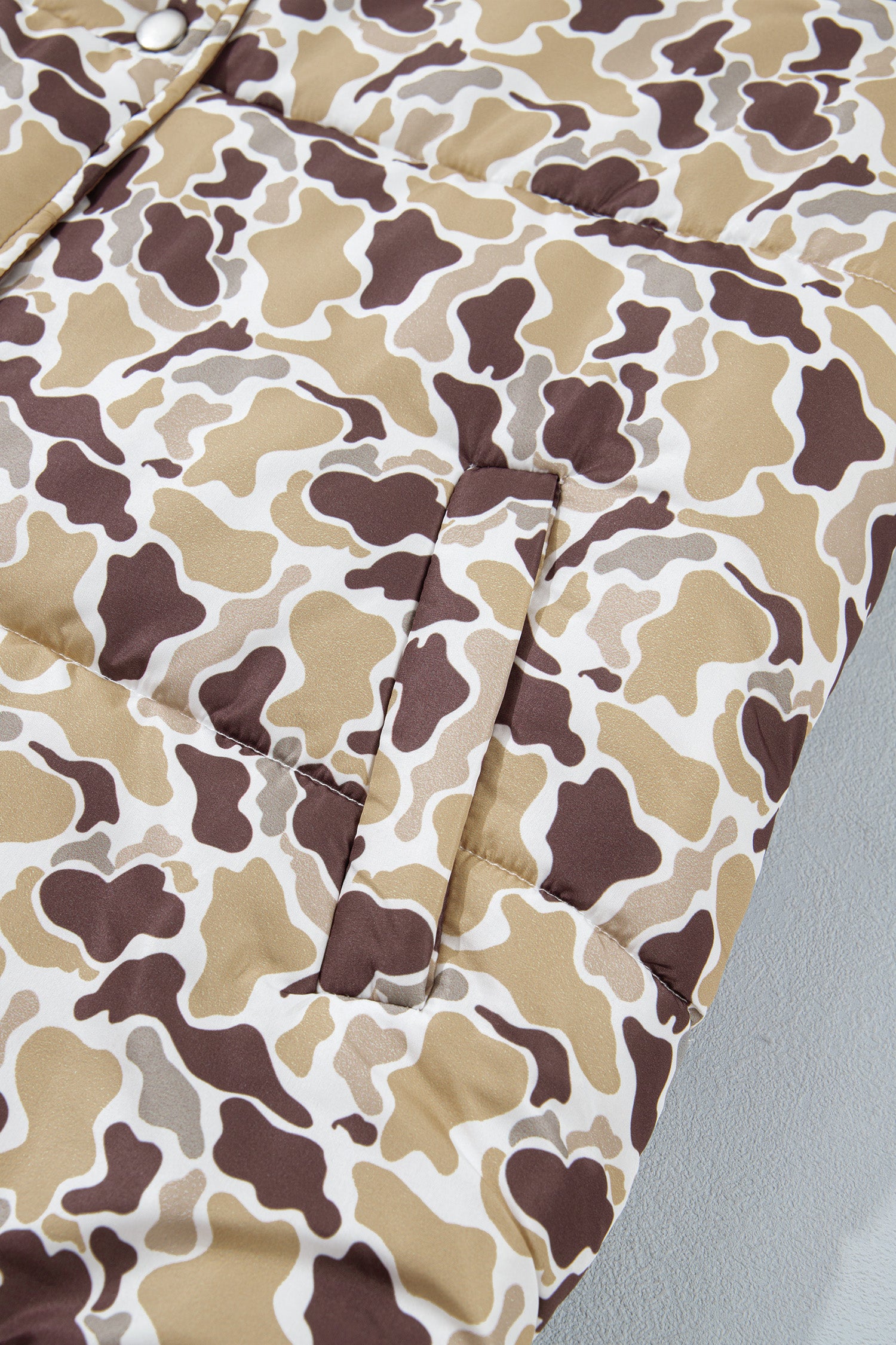 Close-up of a quilted puffer jacket featuring a brown, beige, and white camouflage pattern.