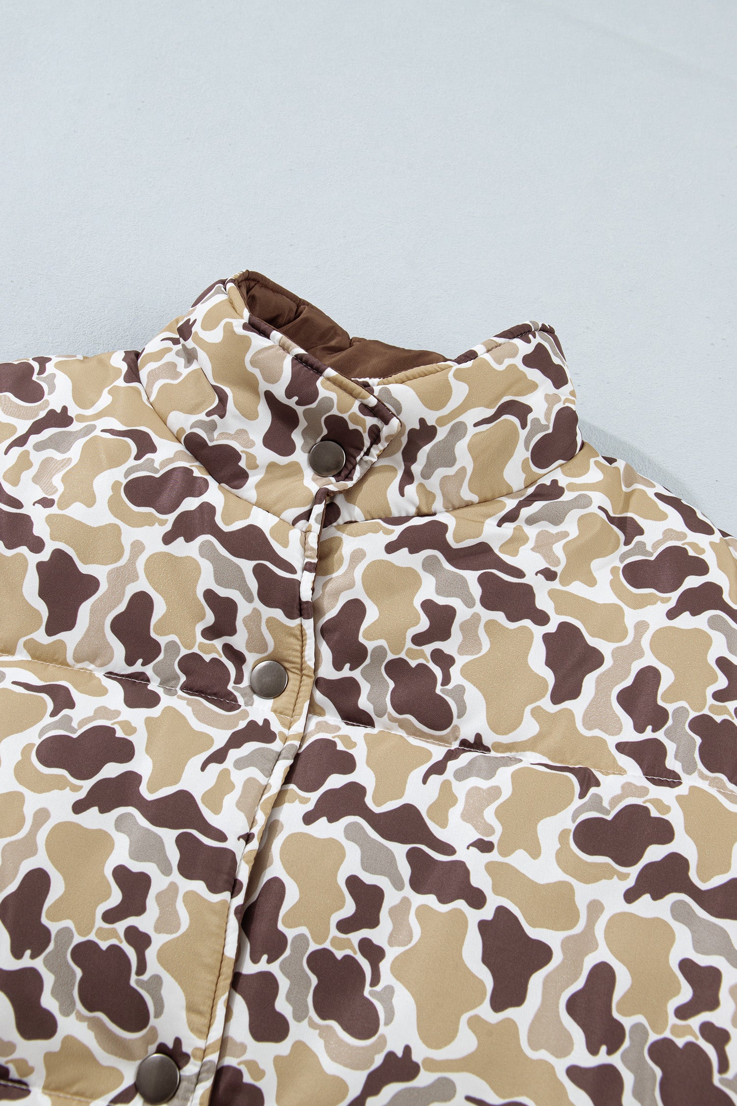 Close-up of brown, beige, and white camouflage puffer jacket with brown collar and snap buttons.