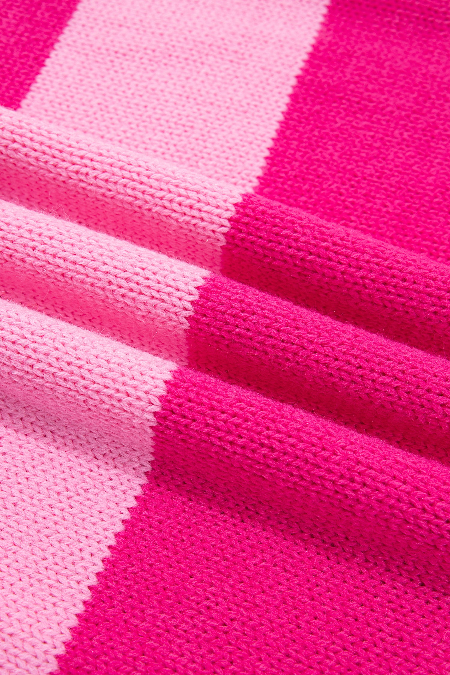 A close-up of a knitted fabric with alternating blocks of bright hot pink and light pink, showing the detailed knit texture and draped folds.