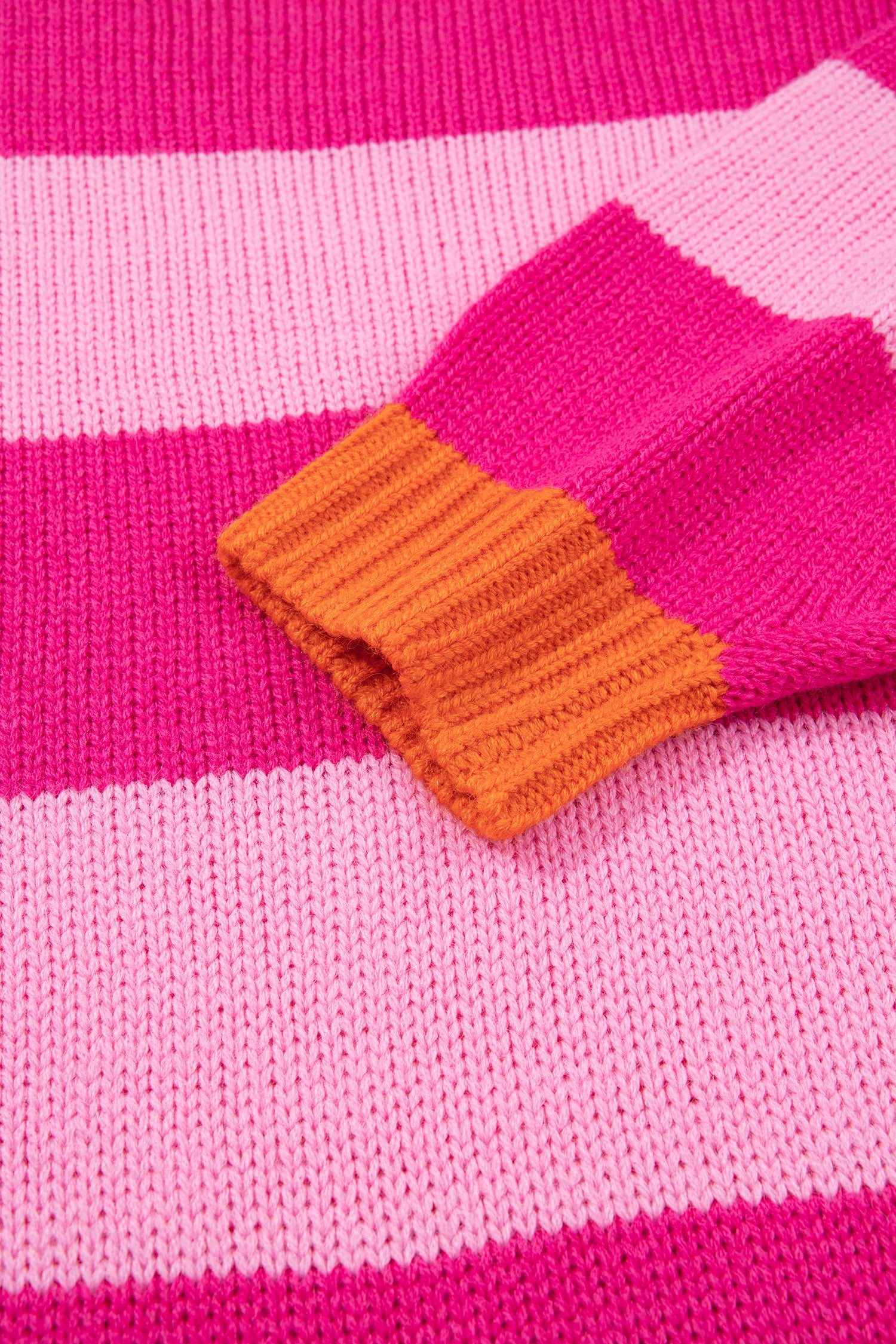 Close-up of a knitted sweater with horizontal pink and light pink stripes and a bright orange ribbed cuff.