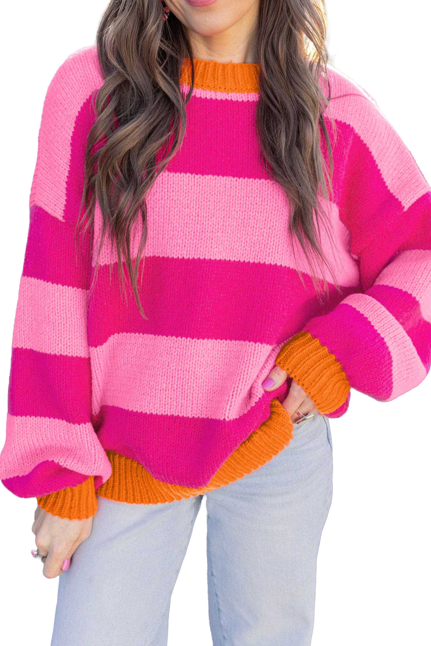 A woman wearing a chunky knit sweater with bold horizontal stripes in hot pink, light pink, and orange, paired with light blue jeans against a plain white background.