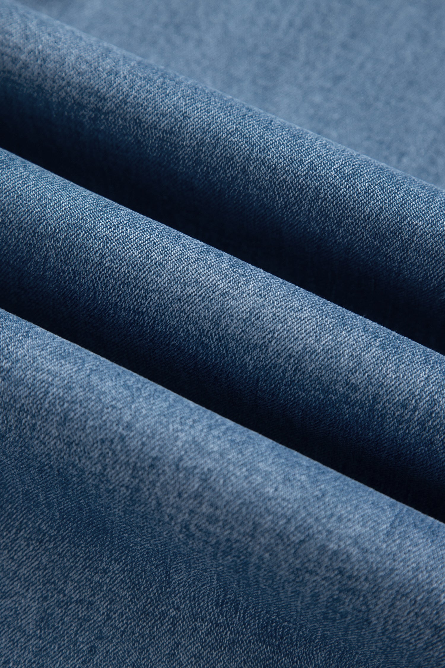 A close-up of folded blue denim fabric showing the textured twill weave and soft shadows between the layers.