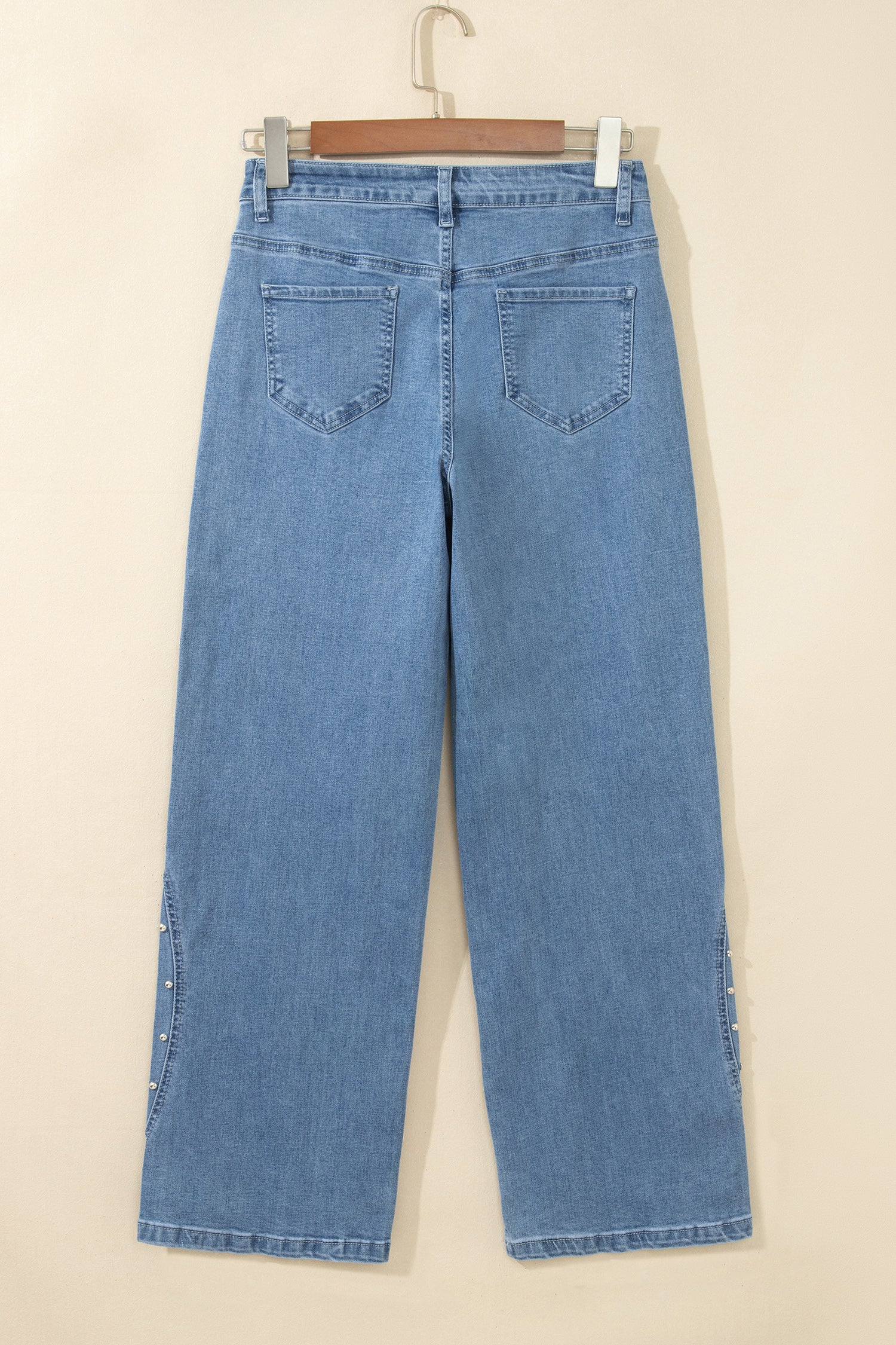 Light blue wide-leg denim jeans shown from the back, hanging on a wooden hanger against a plain beige wall.