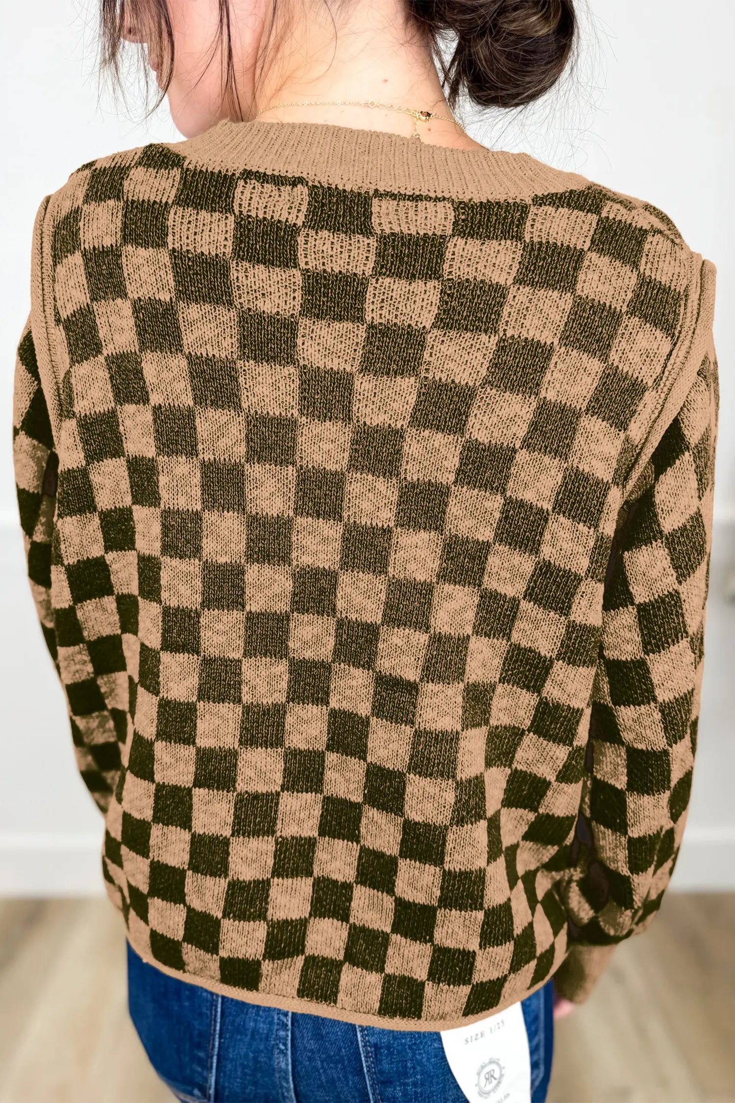 A person viewed from the back wearing a knit sweater with a brown and olive green checkerboard pattern, paired with blue jeans.