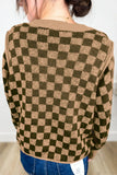 A person viewed from the back wearing a knit sweater with a brown and olive green checkerboard pattern, paired with blue jeans.
