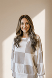 Woman wearing a checkered sweater standing against a neutral background