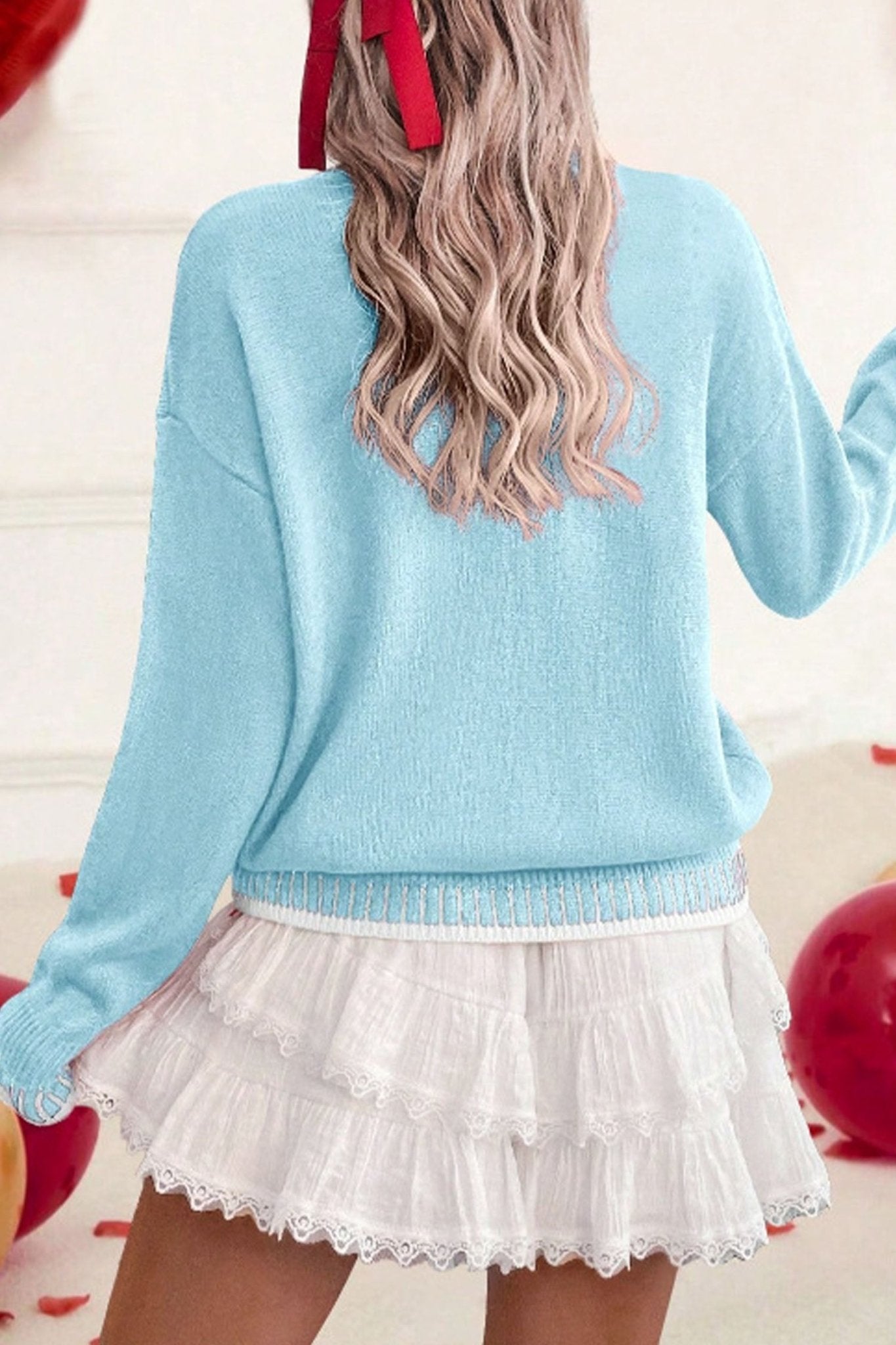 Person wearing a light blue sweater and white lace skirt with red balloons in the background