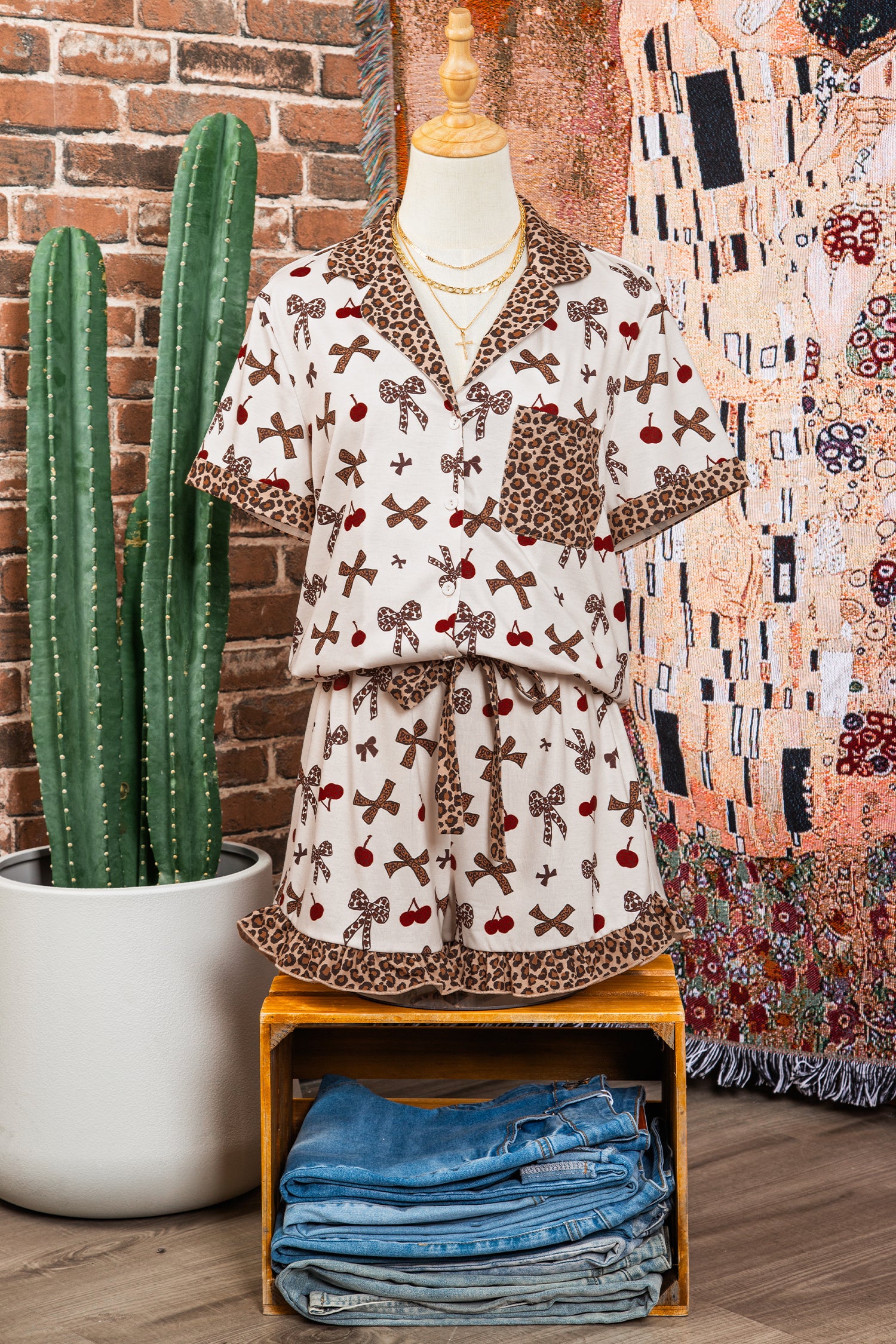 Dress with a pattern on a mannequin next to a potted cactus and folded jeans against a brick wall.