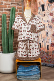 Dress with a pattern on a mannequin next to a potted cactus and folded jeans against a brick wall.