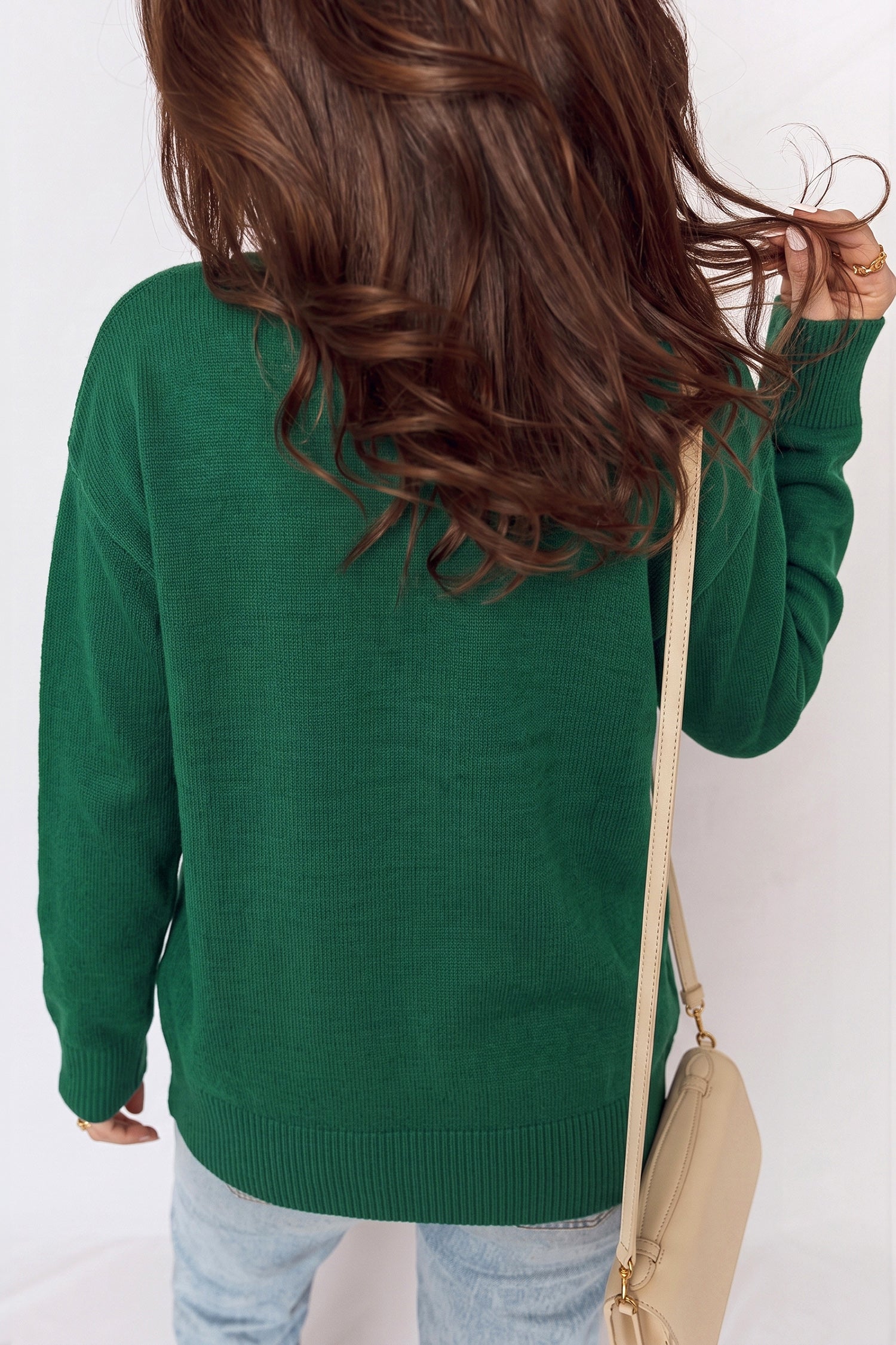 Back view of woman in green knit sweater, light blue jeans, and beige shoulder bag.