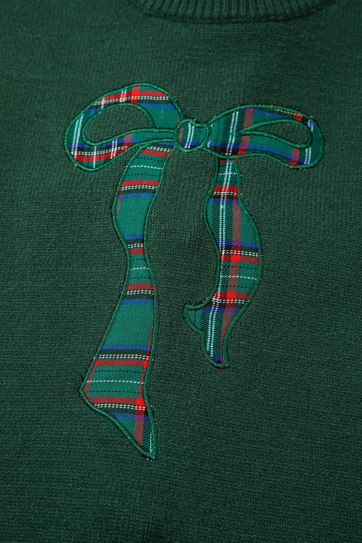 Close-up of dark green sweater with green tartan plaid bow applique on chest.