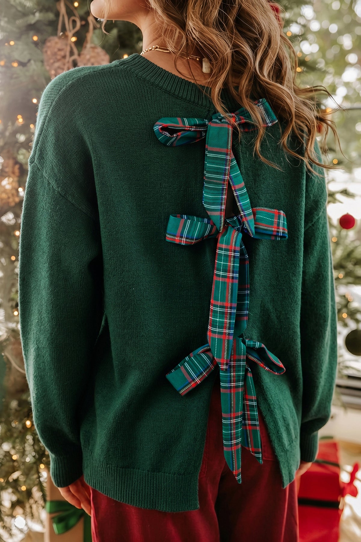 Woman in dark green knit sweater with large plaid ribbon on back.