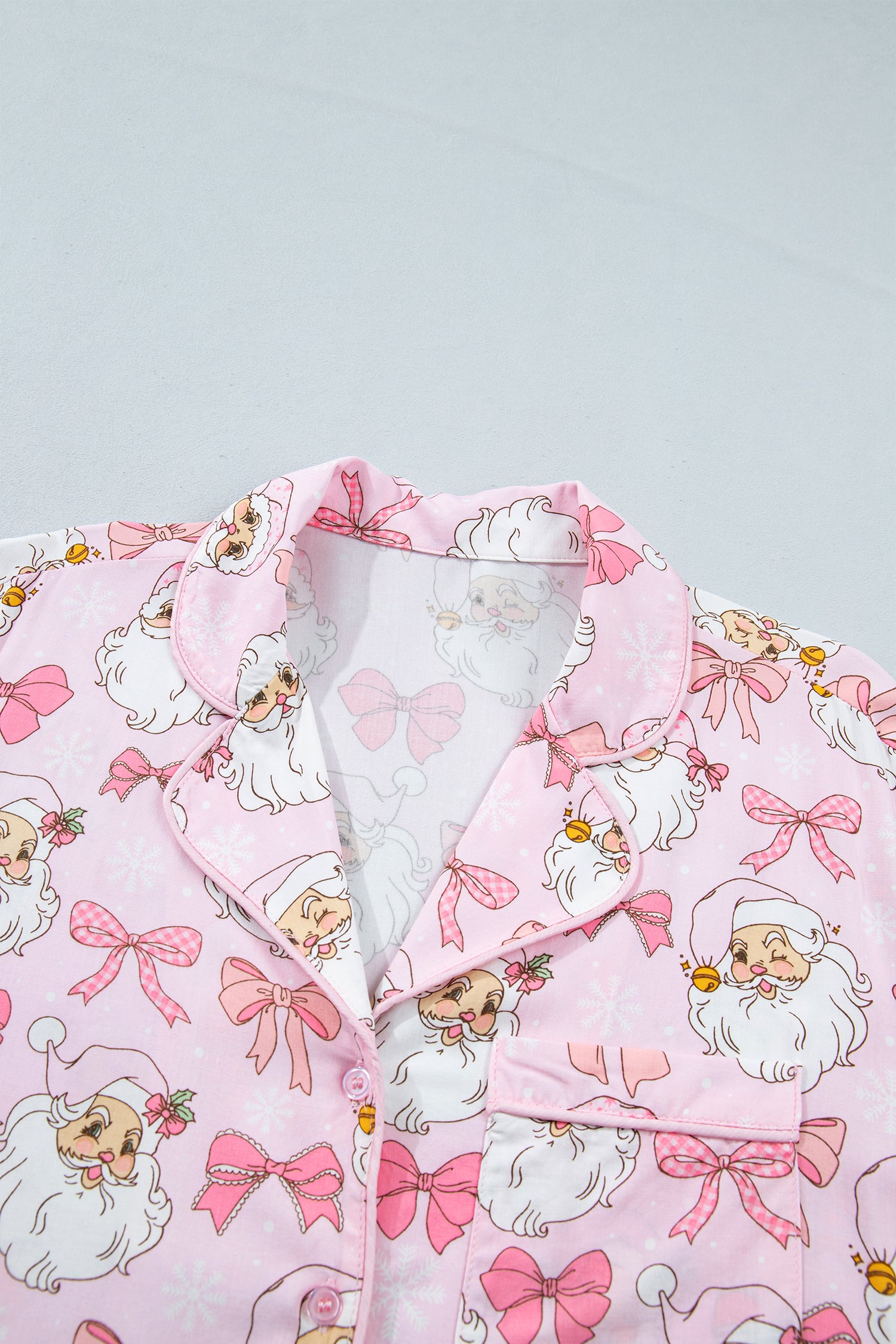 Pink pajama top with a cartoon Santa Claus and pink bow print, shown laid flat against a light gray background.