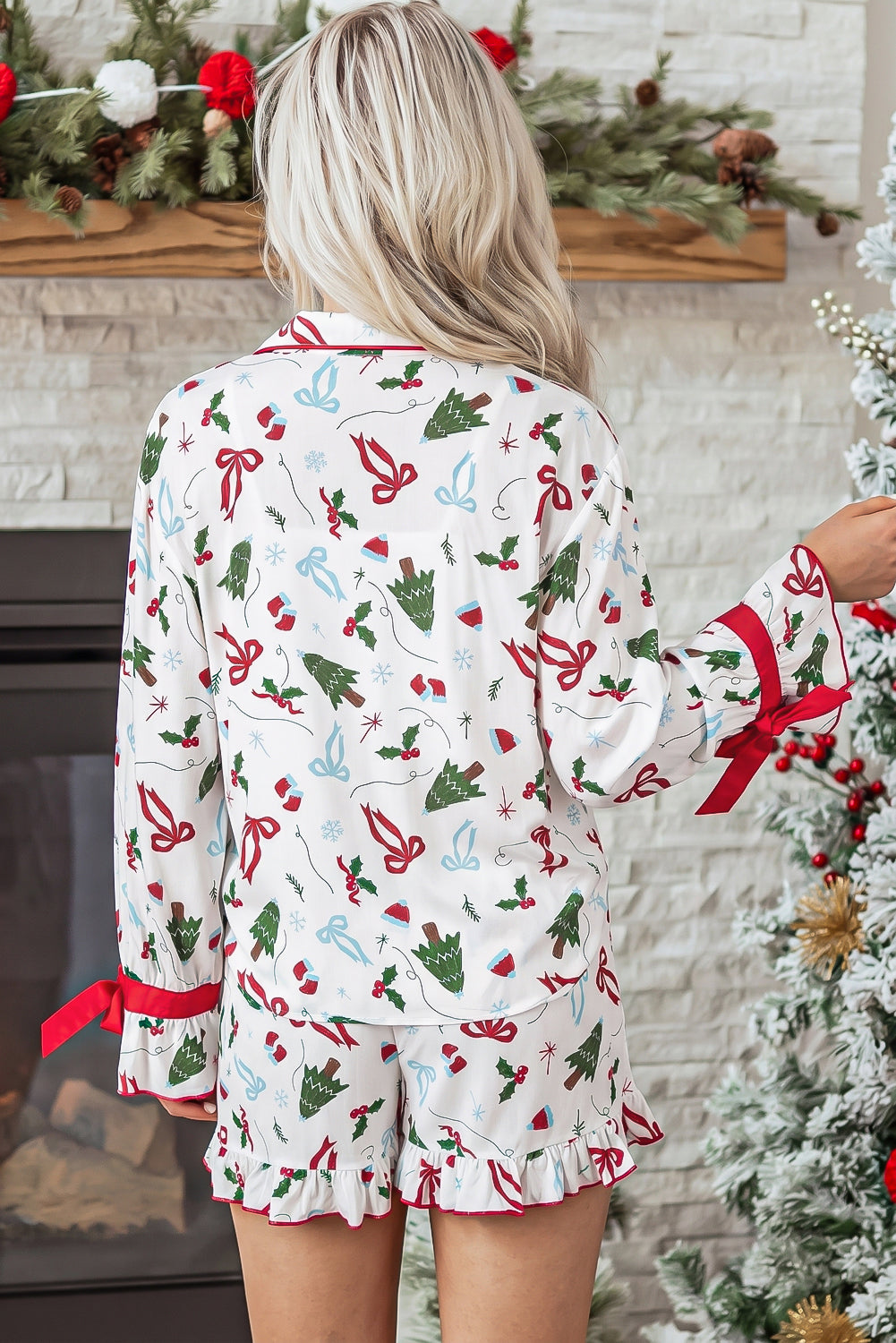 Woman viewed from behind in white Christmas-print pajamas by a decorated tree.