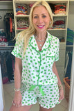 Woman wearing a green and white shamrock patterned pajama set in a room with shelves of folded clothes.