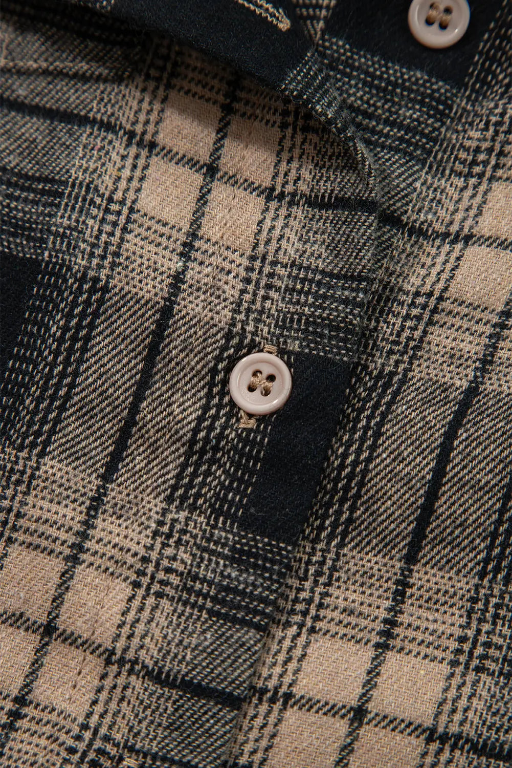 Close-up of a plaid shirt with a button, focusing on texture and pattern.