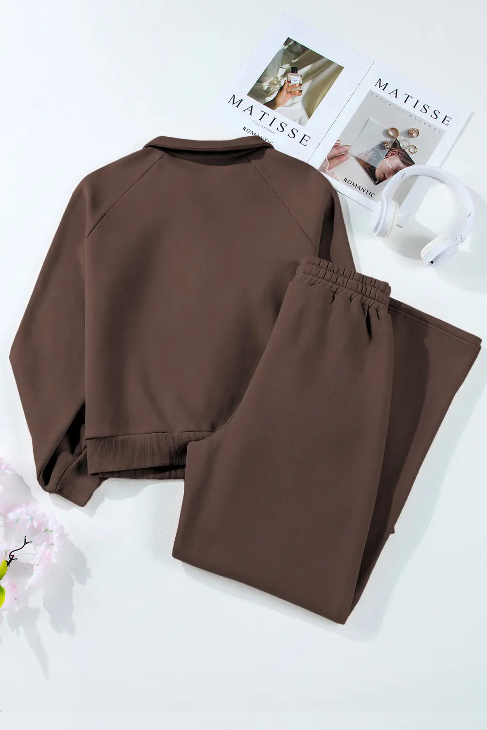 Brown sweatshirt and pants set on a white surface with a magazine in the background.