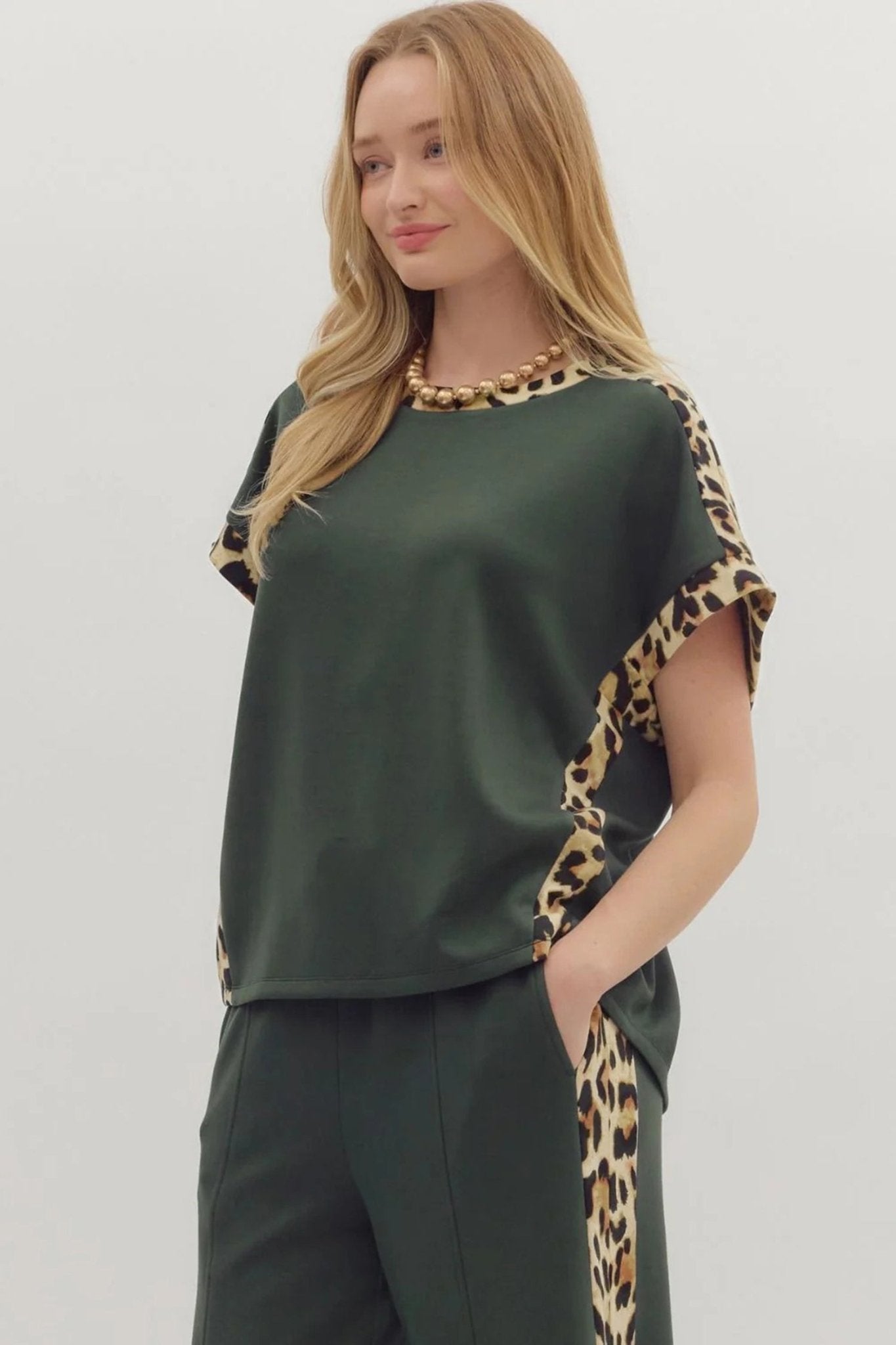 Woman wearing a green top with leopard print sleeves and pants on a white background
