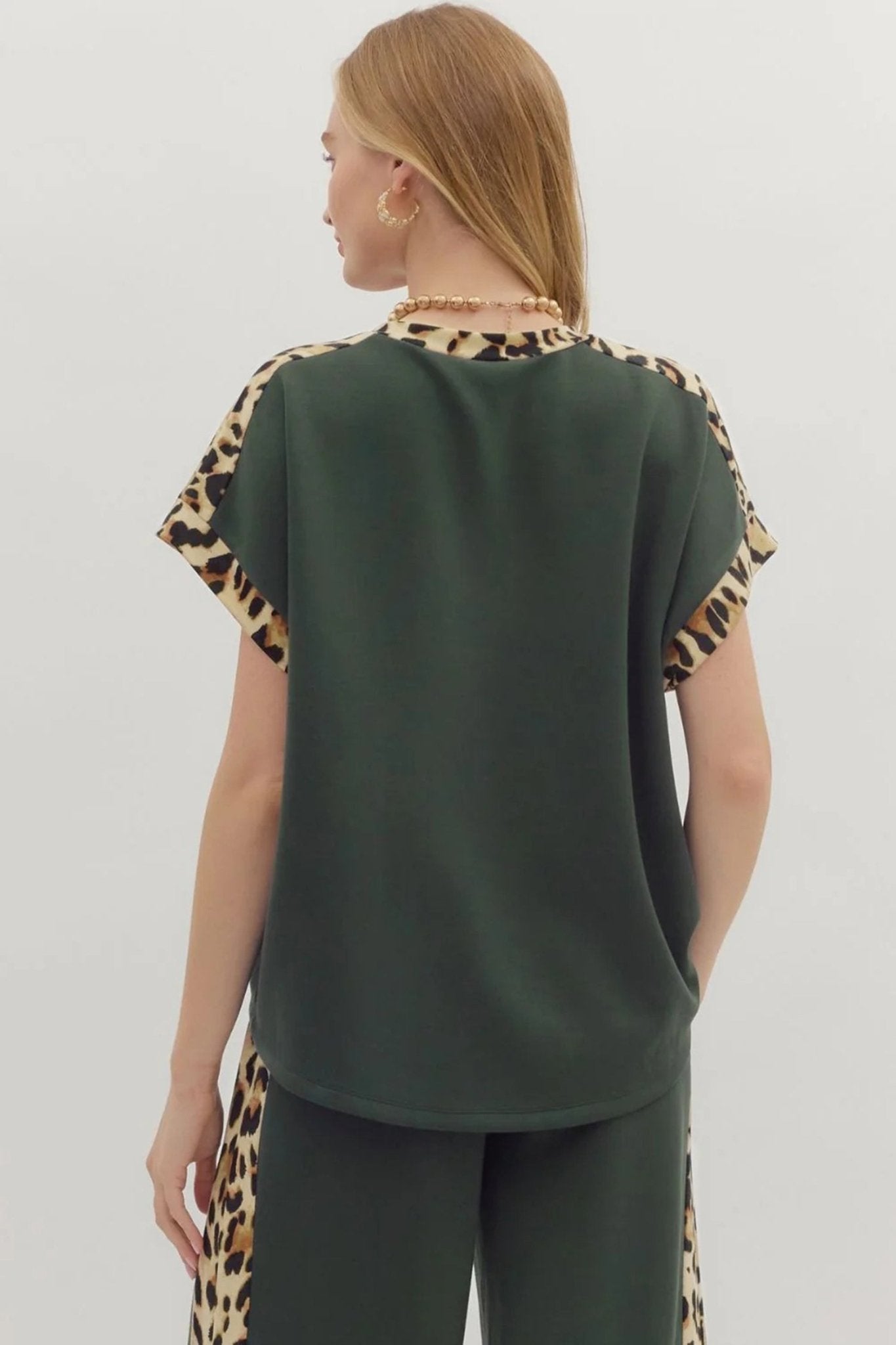 Person wearing a green top with leopard print sleeves and pants on a white background