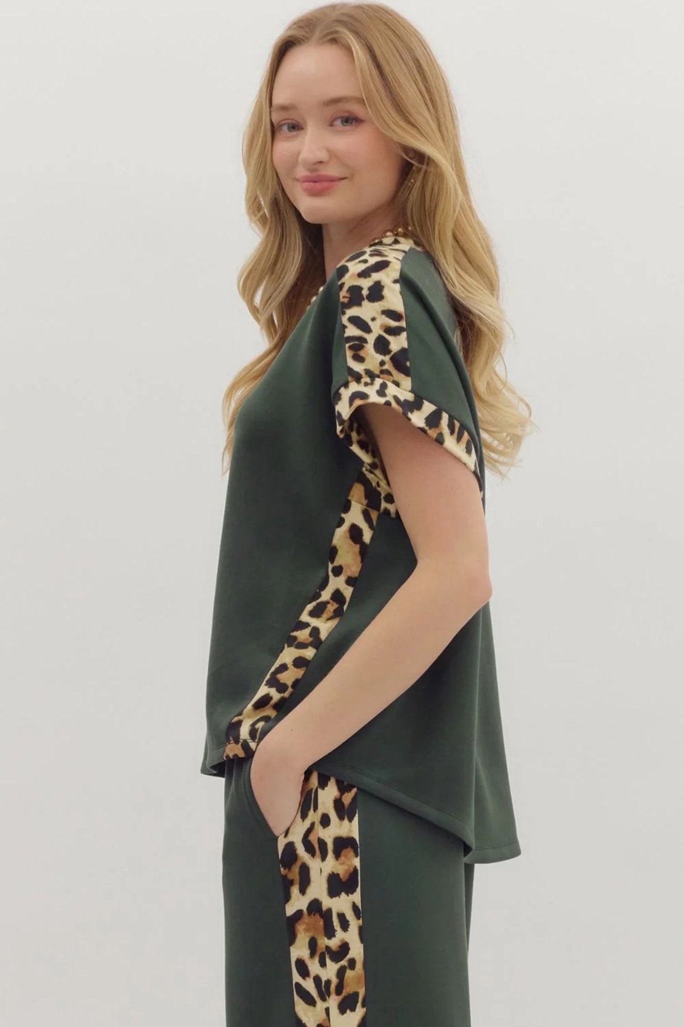 Woman wearing a green dress with leopard print accents on a plain background