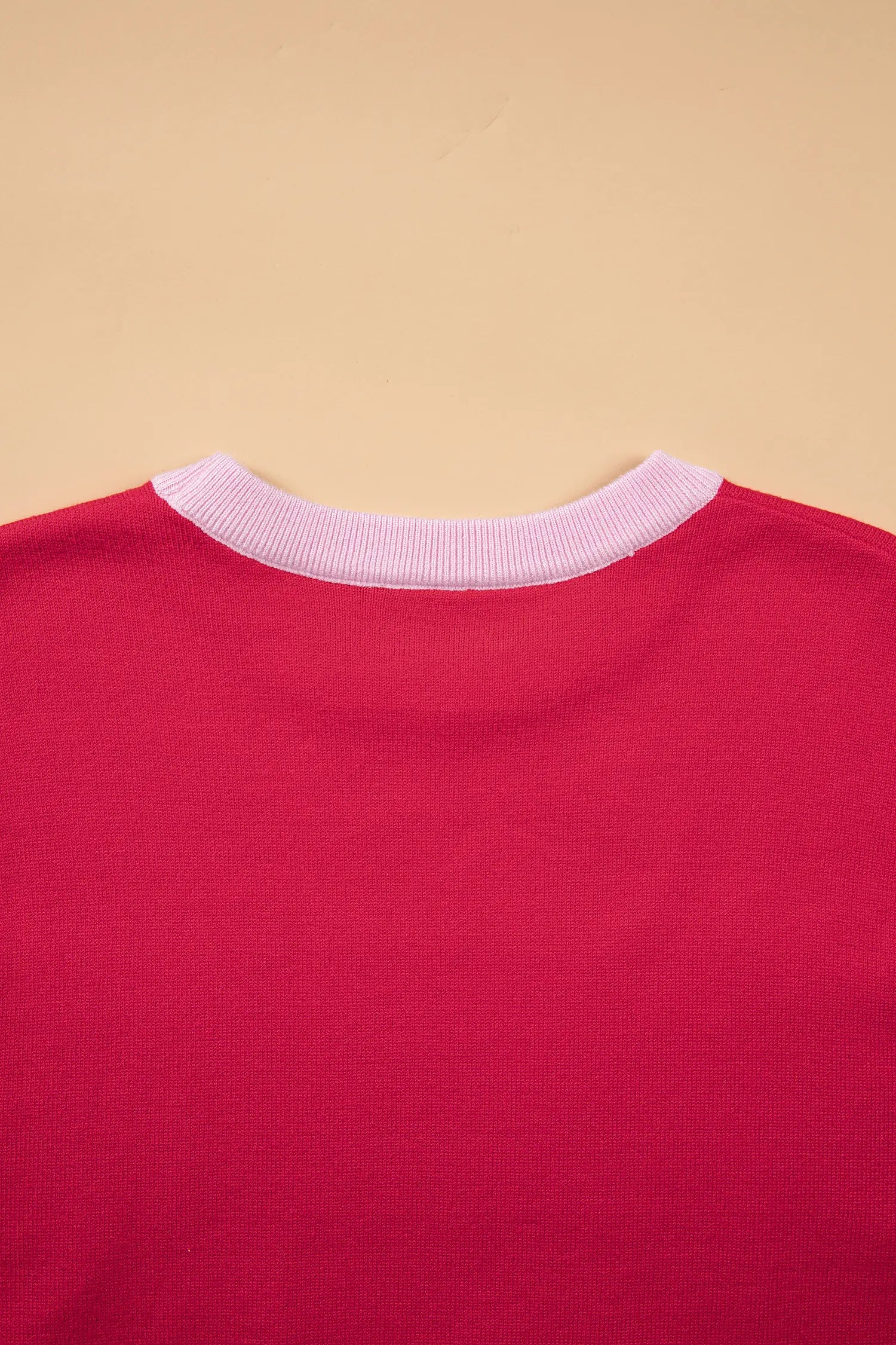 Close-up of the back of a bright pink-red t-shirt with a contrasting light pink ribbed crew neck, set against a solid beige background.