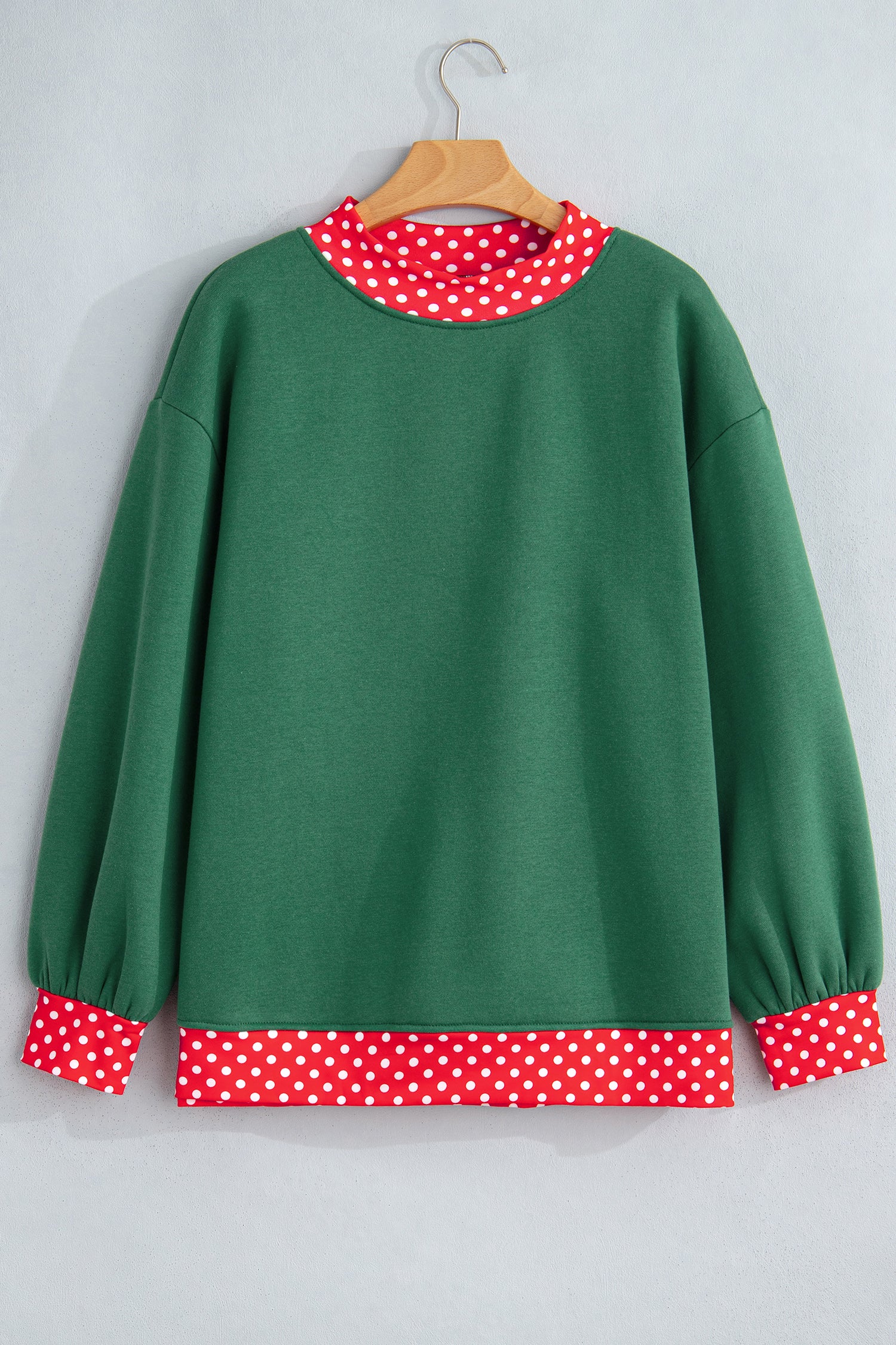 Green sweatshirt with red-white polka-dot trim at neck, cuffs, and hem on hanger.