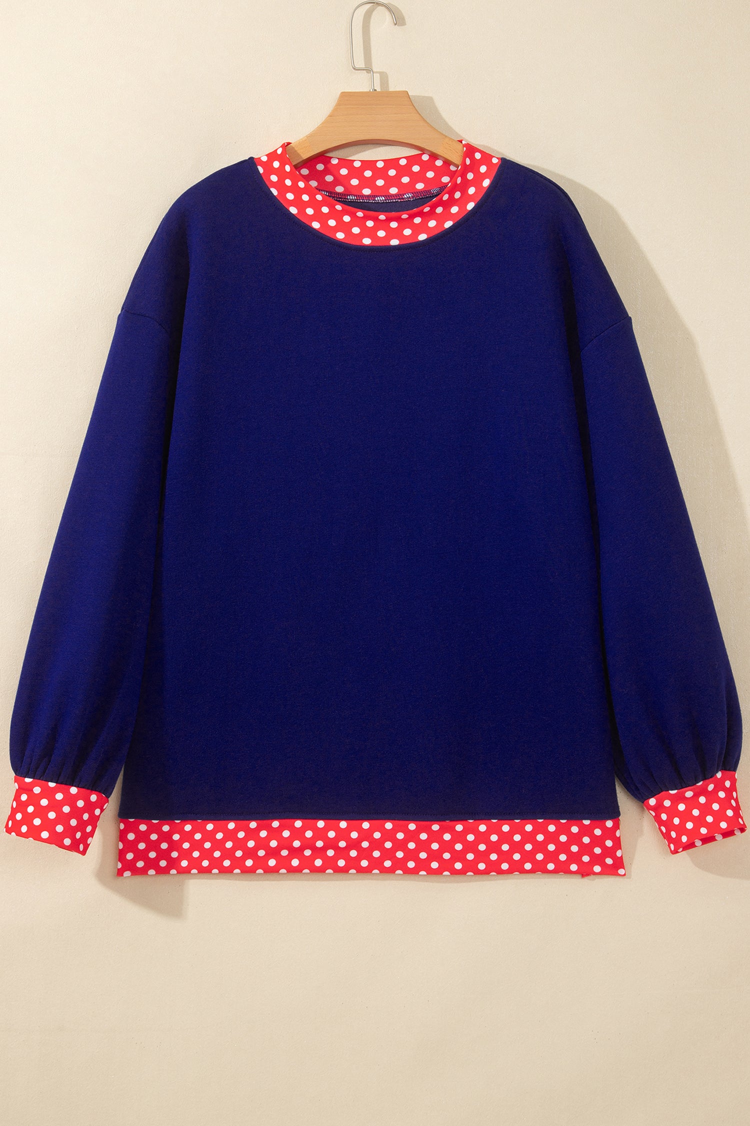 Navy blue sweater with red-white polka-dot trim on wooden hang.