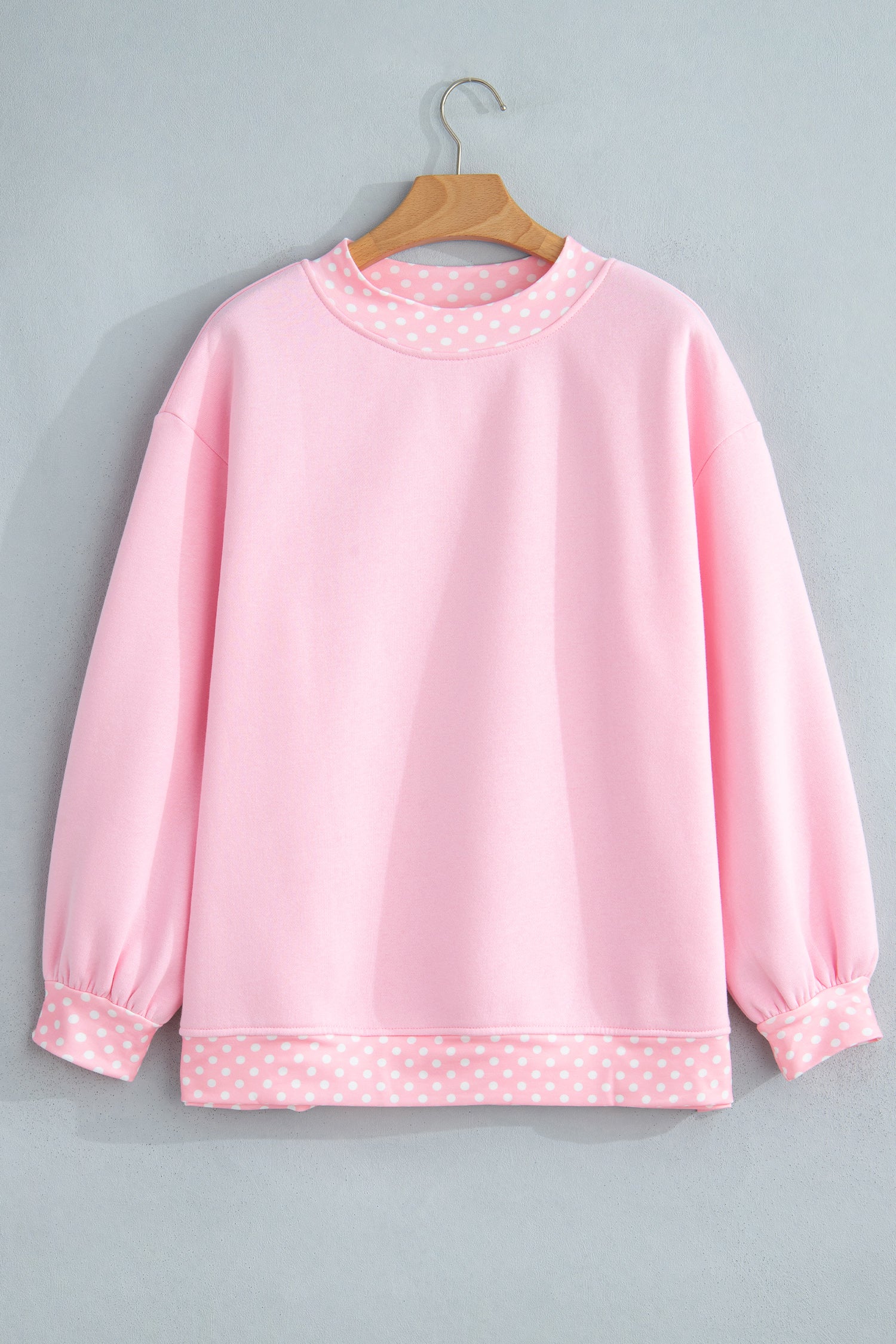 Light pink sweatshirt with pink-white polka-dot trim on wooden hanger.
