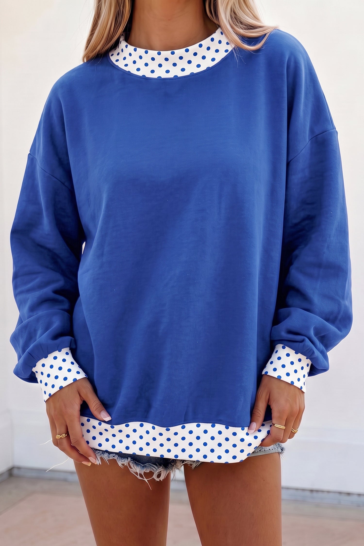 Woman in royal blue sweatshirt with white polka-dot trim and denim shorts.