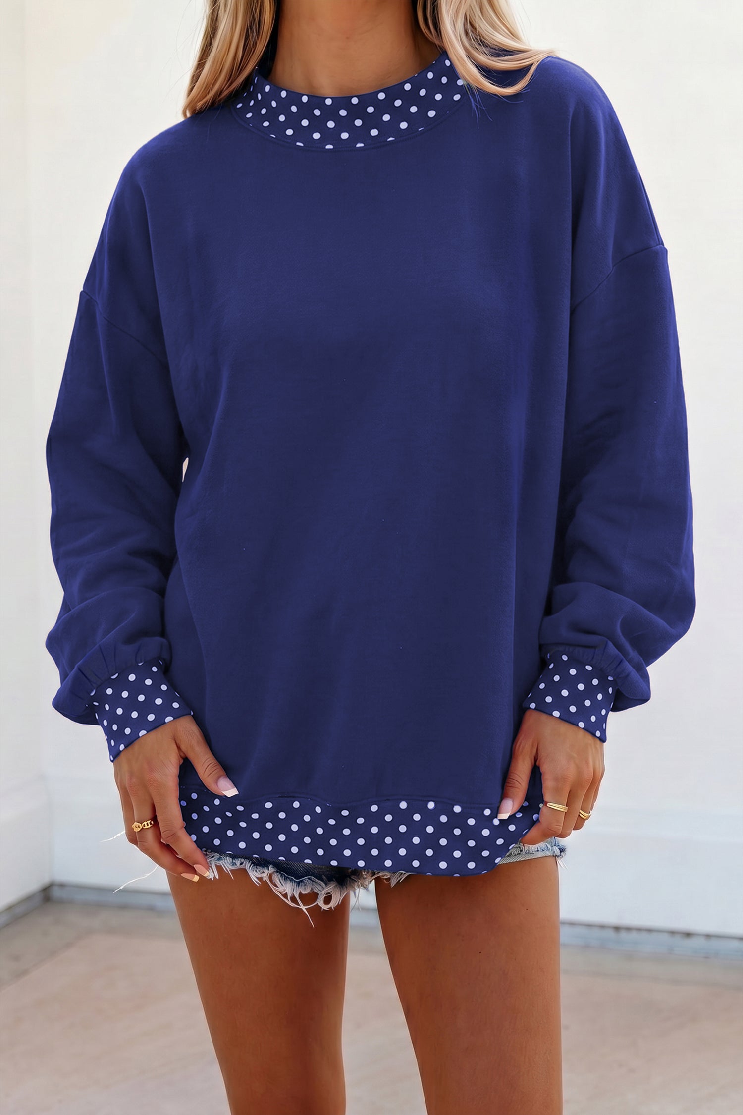 Woman in oversized navy sweatshirt with white polka-dot trim and denim shorts.