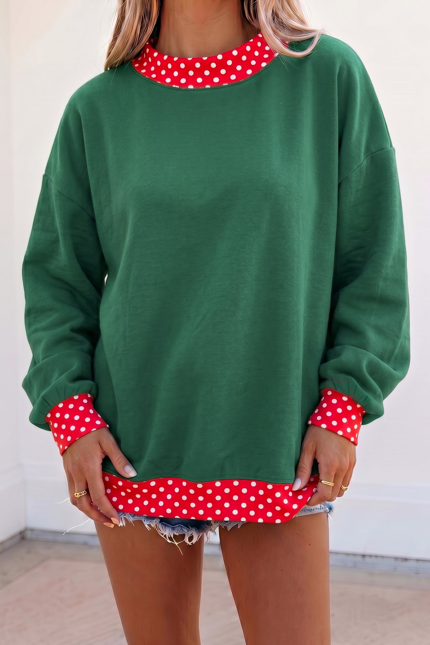 Woman in green sweatshirt with red-white polka-dot trim and denim shorts.
