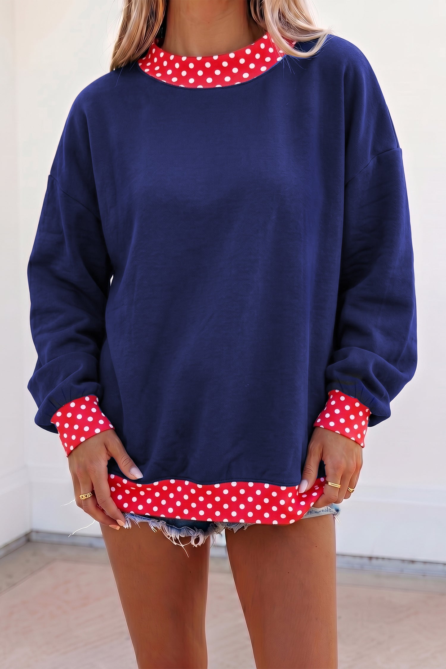 Woman in oversized navy sweatshirt with red-white polka-dot trim and denim short.
