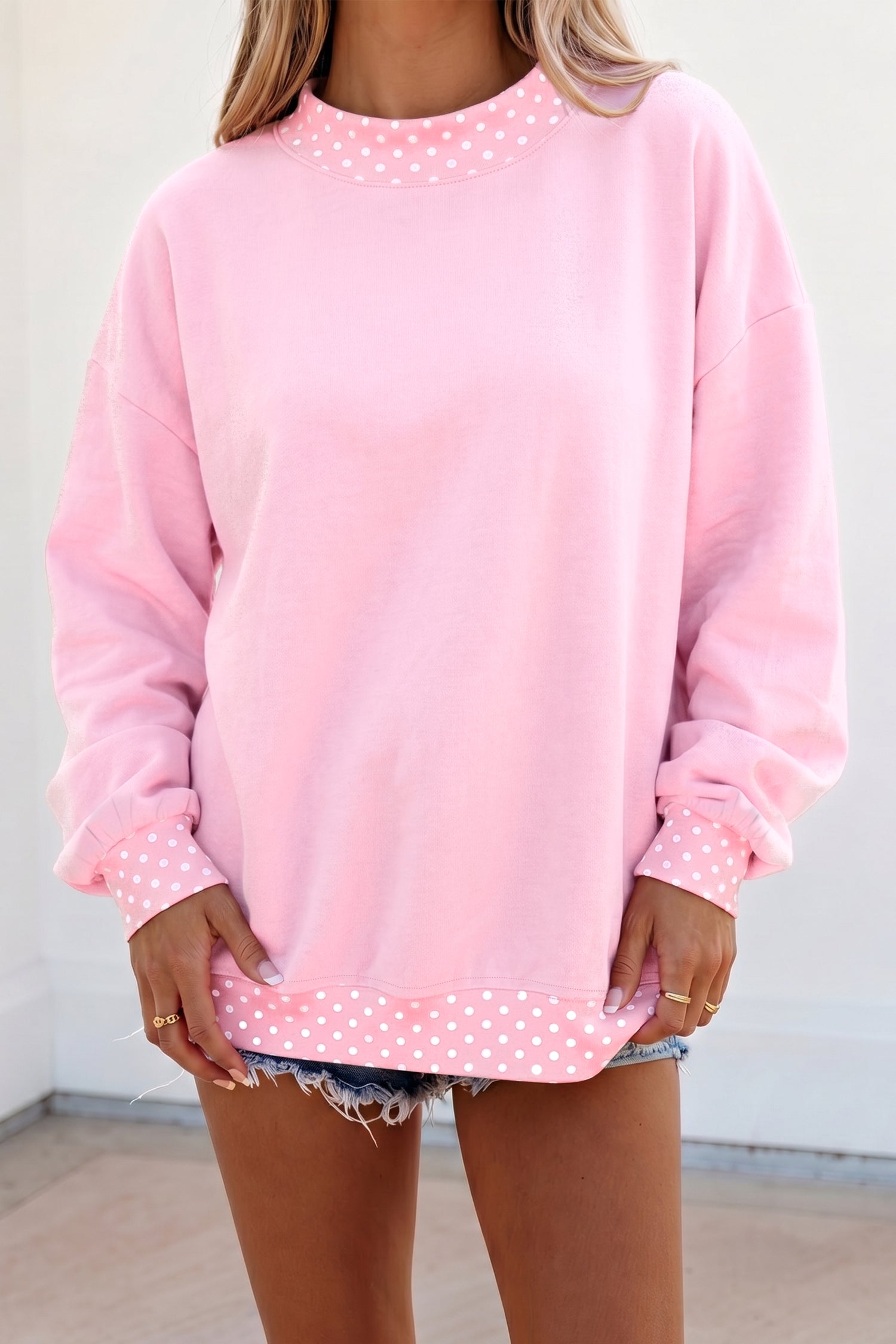 Woman in light pink sweatshirt with white polka-dot trim and denim shorts.