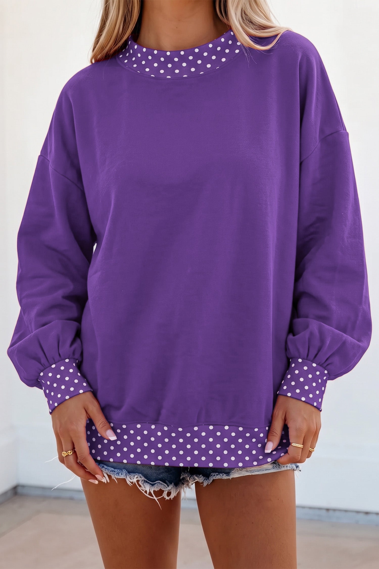 Woman in purple sweatshirt with white polka-dot trim and denim shorts.