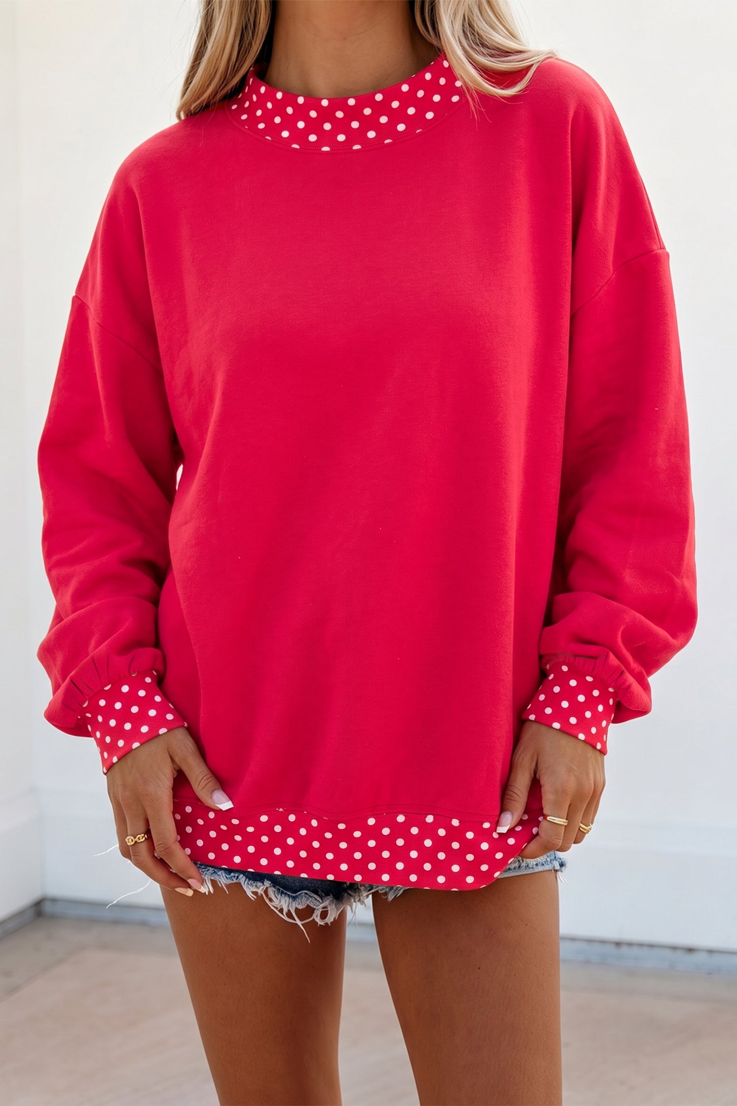 Woman in bright red sweatshirt with white polka-dot trim and denim shorts.