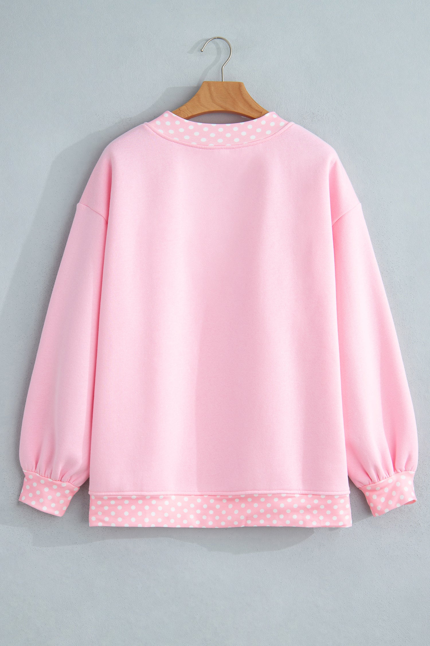Light pink sweatshirt with contrasting pink-white polka-dot trim on hanger.