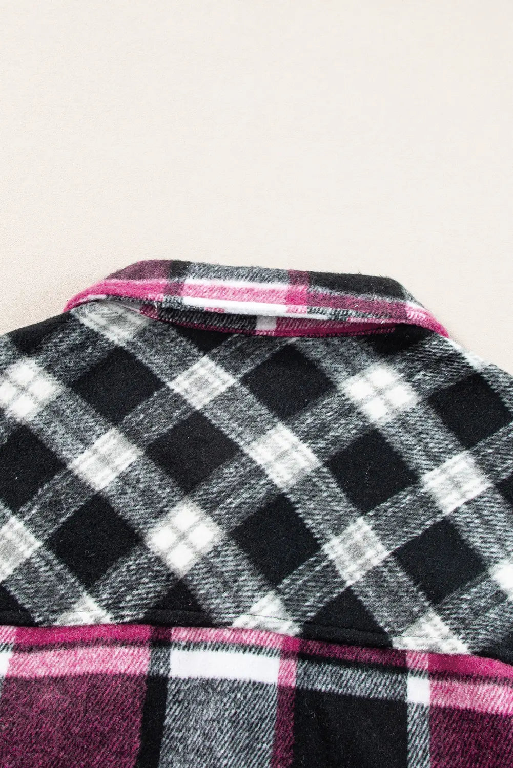 Close-up of a plaid fabric with black, white, and pink colors on a light background.