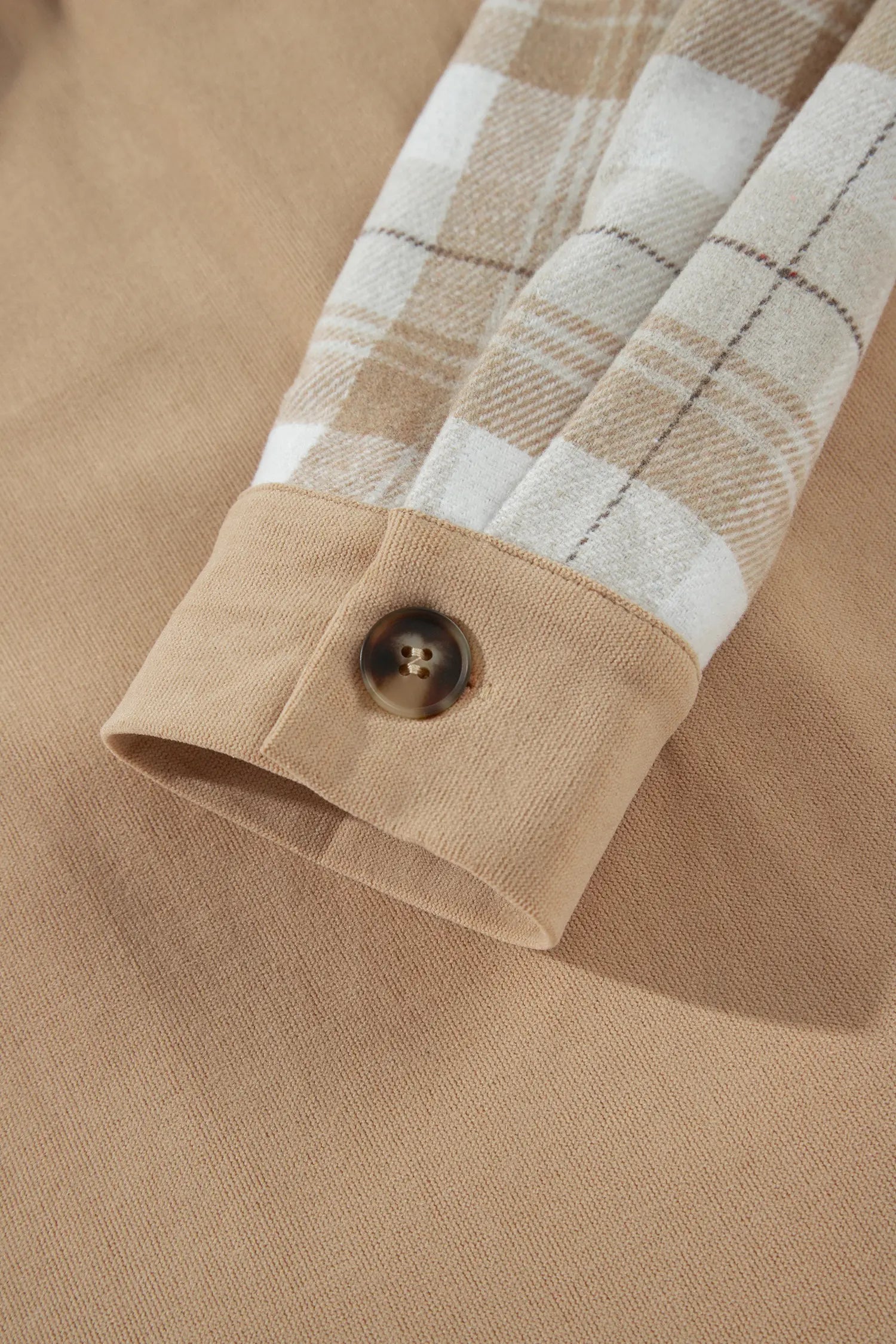 Close-up of a beige long-sleeve shirt with a plaid pattern on the sleeve and a buttoned cuff.