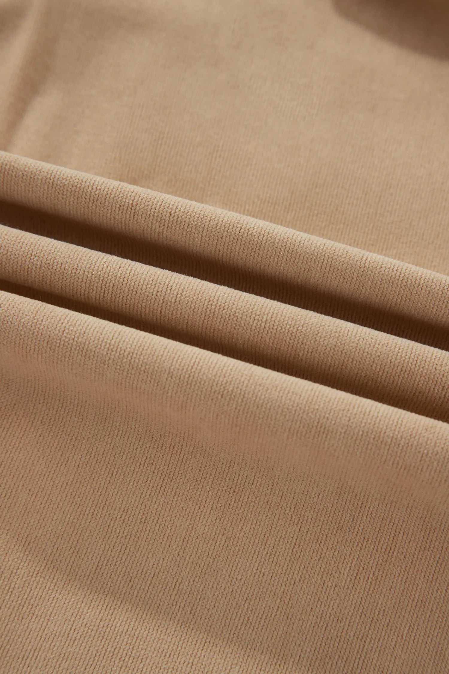 A close-up of draped beige knit fabric with soft folds showing the fine ribbed texture.