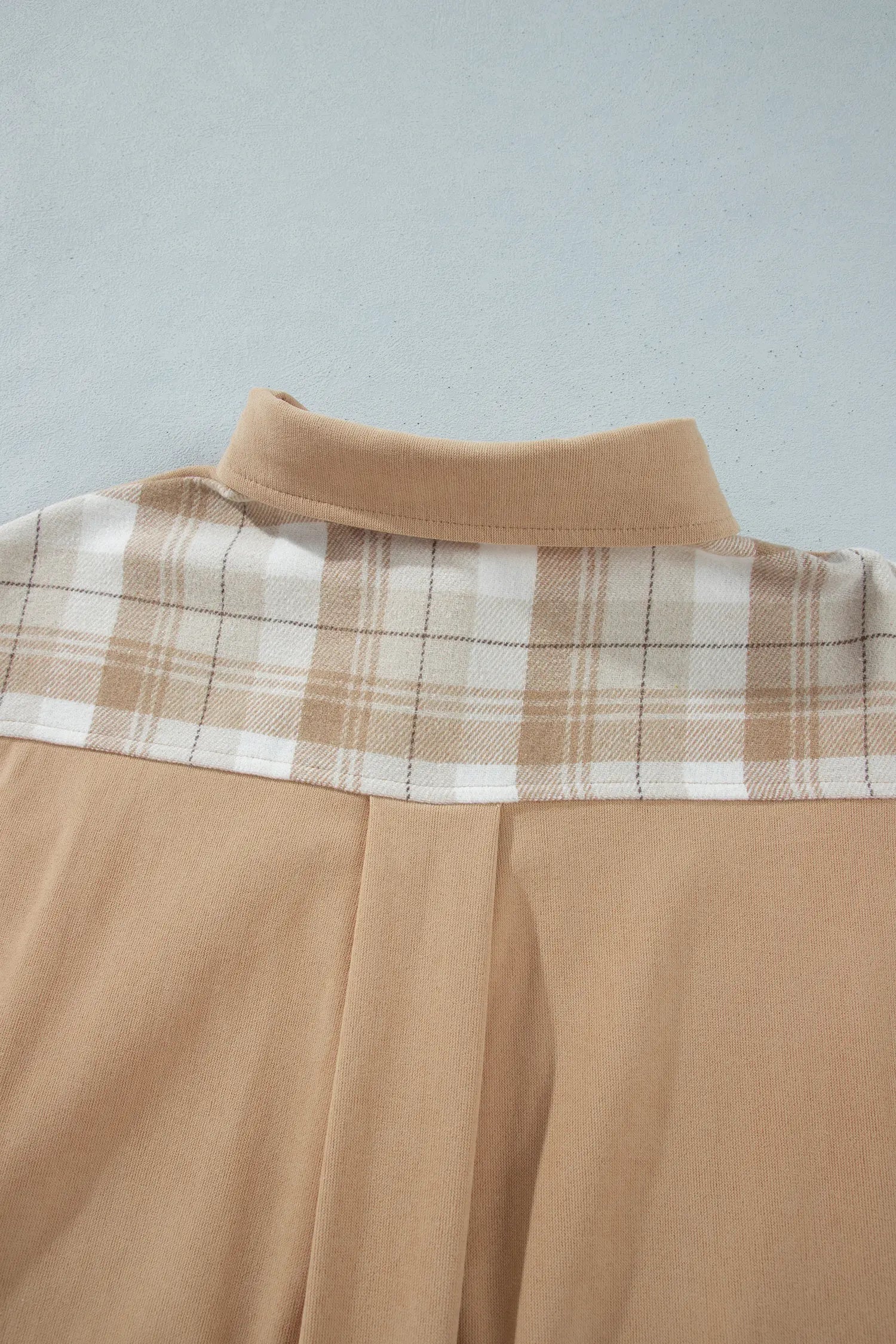 Close-up of a beige and white plaid shirt collar with a solid beige body, laid flat against a light gray background.